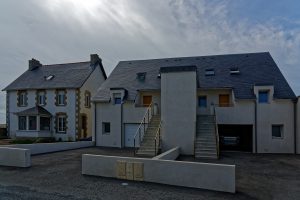 Man dreht sich um und sieht den Eingang zum Ferienhaus. Hinter dem Gebäude liegt das Meer